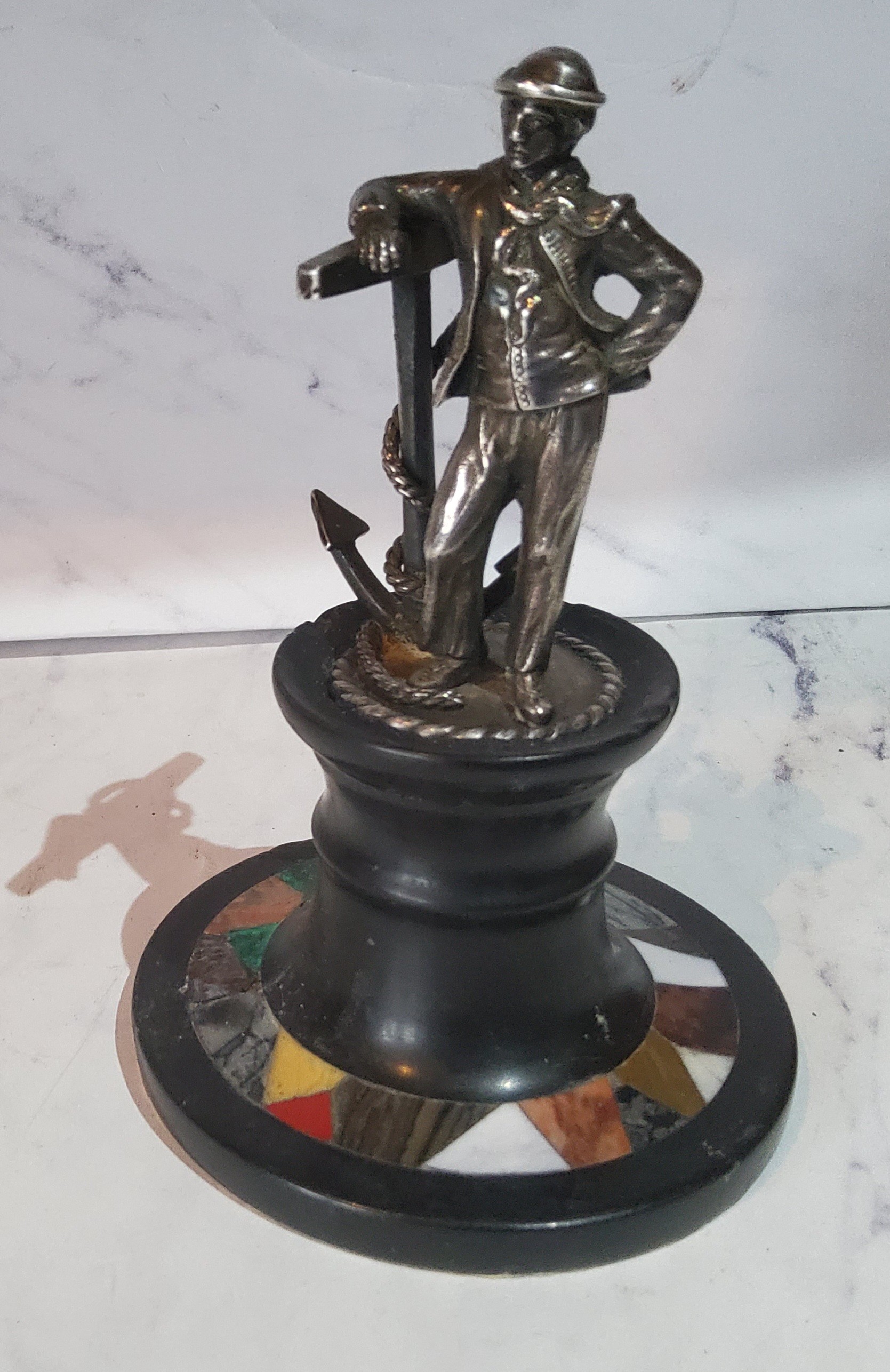 A silver coloured metal figure, of a sailor standing by an oversized anchor, pietra dura capstan