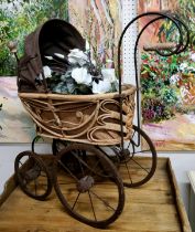 A wrought iron and woven wicker dolls pram / stroller; basket with decorative artificial flowers