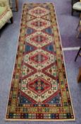 An early 20th century Kazak runner in vivid tones of maroon, blue and ivory, 340cm x 91cm