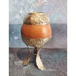 A South American silver coloured metal mounted calabash gourd mate cup, loft legs, 14cm high