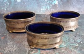 A set of three George V silver open oval  salts, pierced bands, blue glass liners, bun feet, 6.5cm