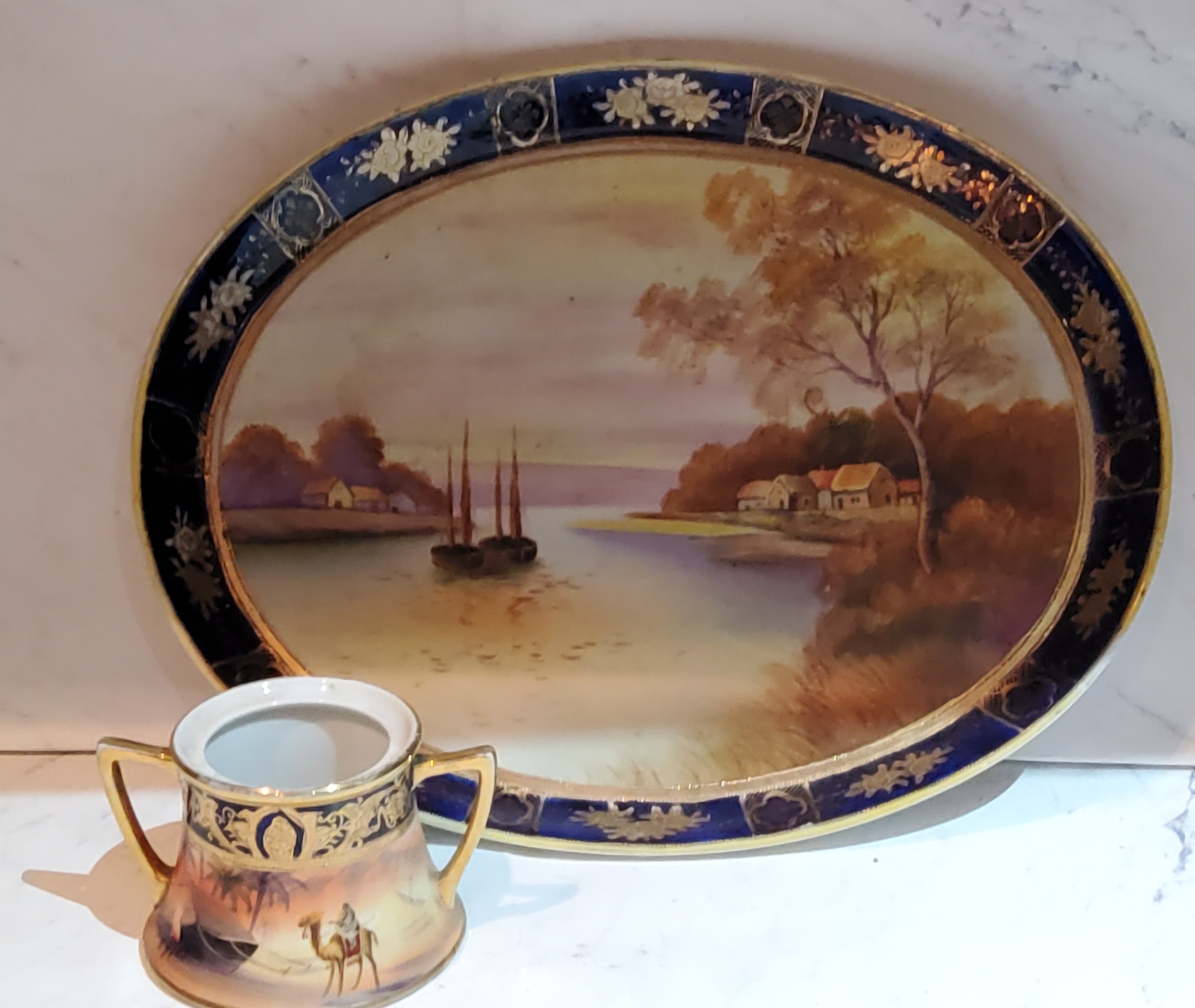 A Noritake oval cabaret tray, painted with riverscape, cobalt banded border, 32cm wide, printed - Image 2 of 2