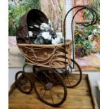 A wrought iron and woven wicker dolls pram / stroller; basket with decorative artificial flowers