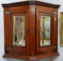An Edwardian Sheraton Revival canted corner cupboard, dental cornice above mirror panelled doors