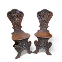 An unusual pair of '17th Century' Continental sgabello hall chairs, the back profusely carved with