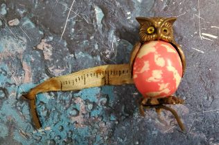 An Edwardian novelty tape measure, as an owl, 'marbled' pink body, 4.25cm high, c.1910