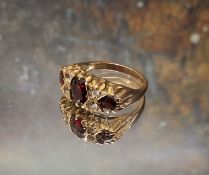 A 9ct gold garnet and diamond gypsy ring, the central oval garnet flanked by two round garnets