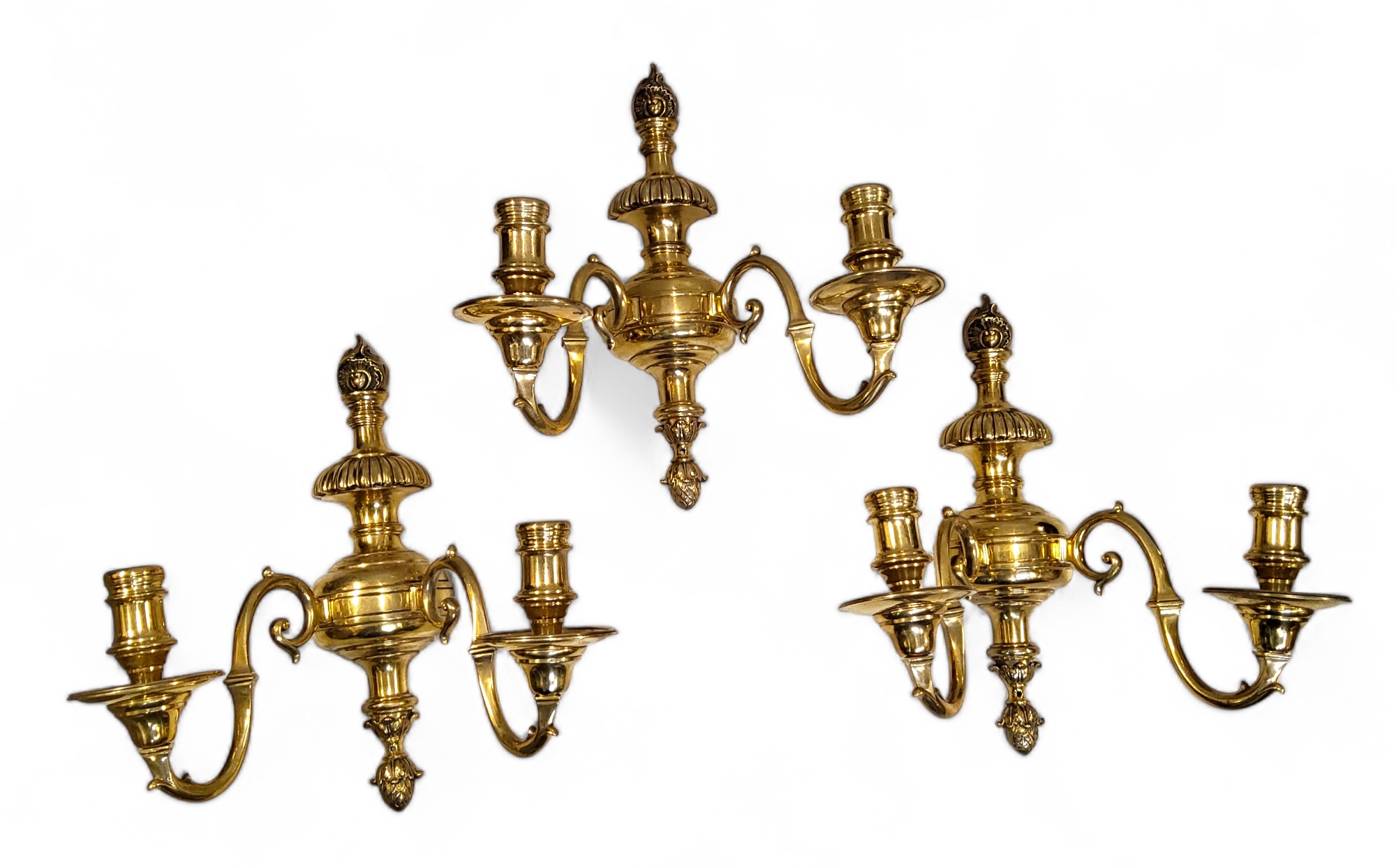 A set of three brass two light wall sconces, reel shaped sconces, leafy finials, 34cm high