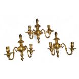 A set of three brass two light wall sconces, reel shaped sconces, leafy finials, 34cm high