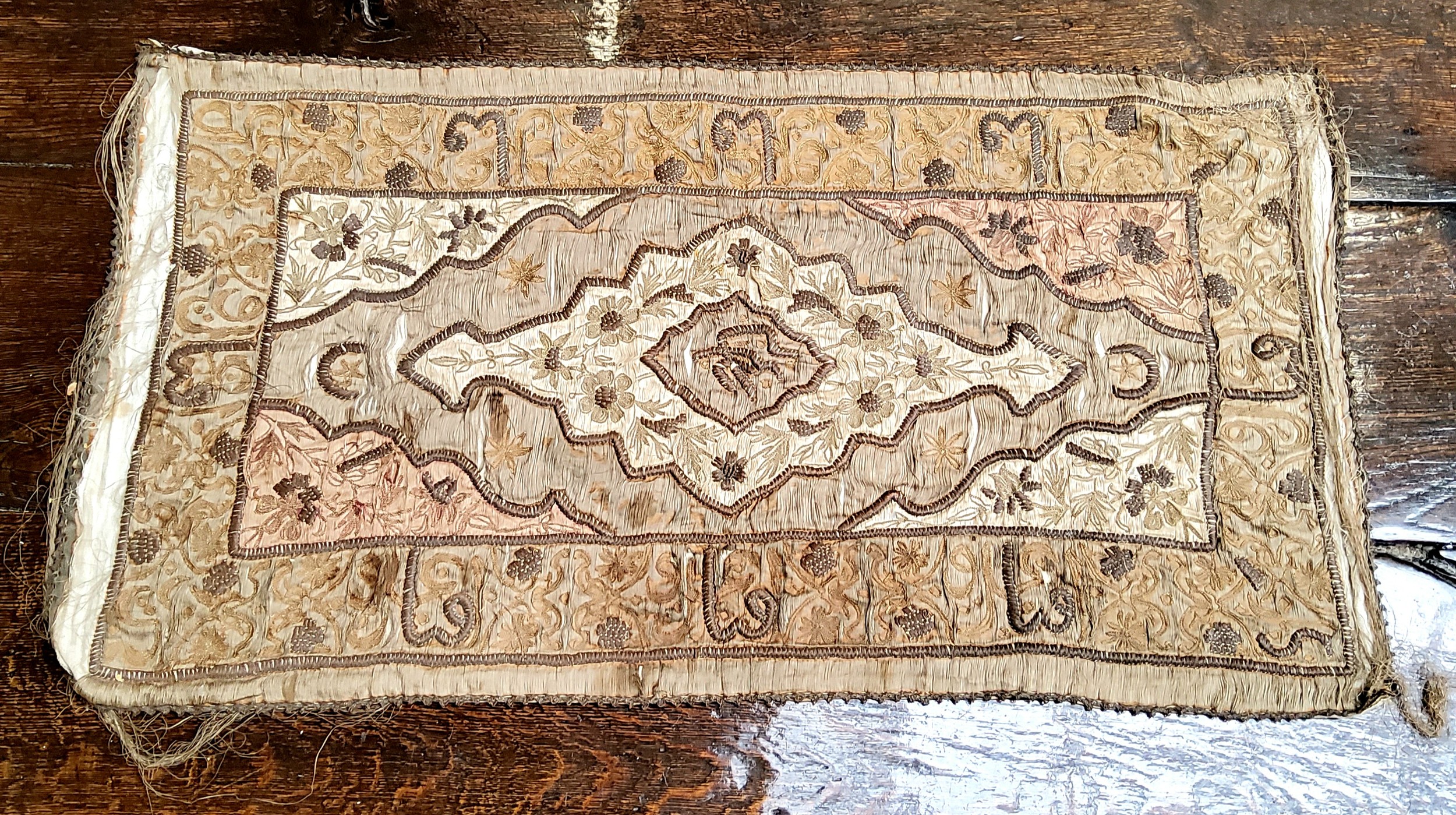 A Persian silk panel, embroidered with central shaped medallion, script, flowers and foliage, in