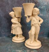 A pair of Belleek figural spill vases, modelled as a boy and a girl  holding baskets, 21.5cm high,