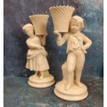 A pair of Belleek figural spill vases, modelled as a boy and a girl  holding baskets, 21.5cm high,