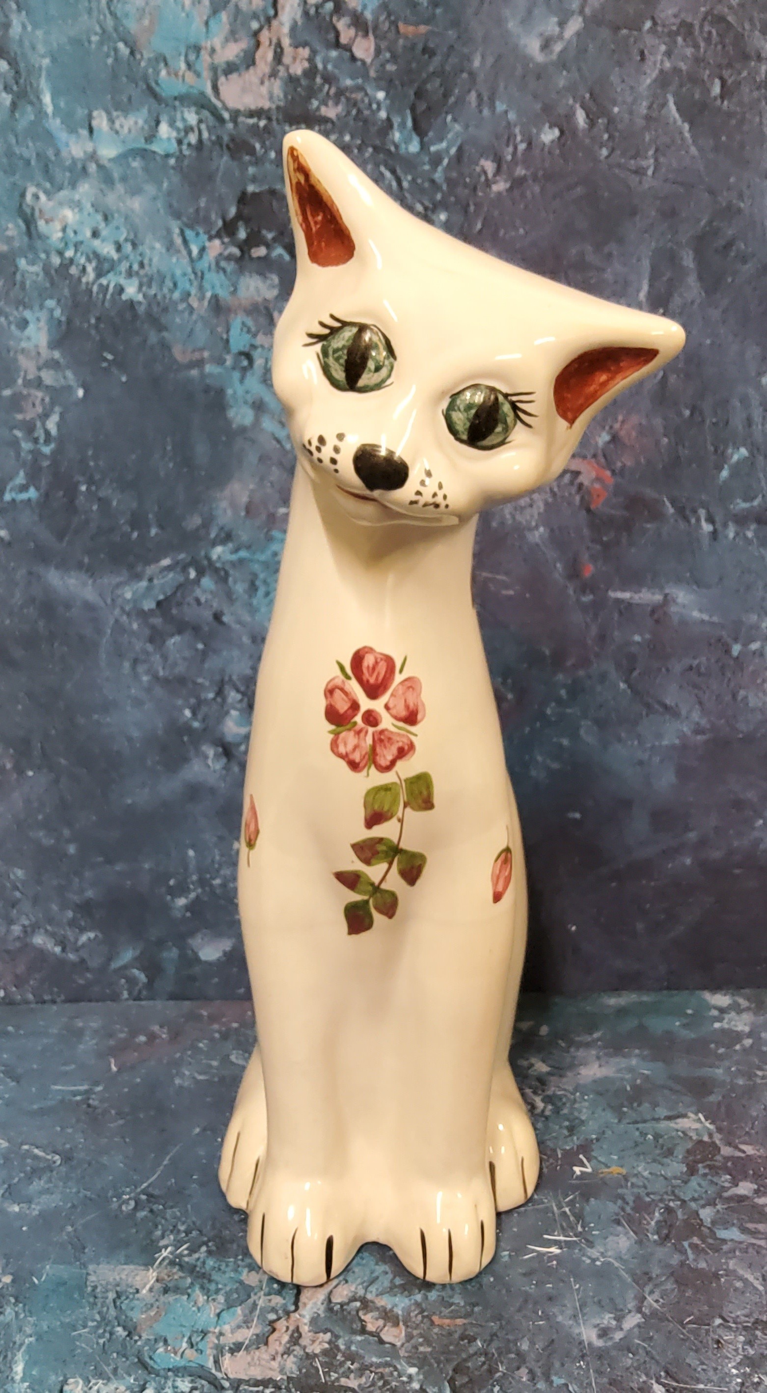 A C.H. Brannnam (Barnstaple) pottery cat,  seated, with head tilted, painted with stylised