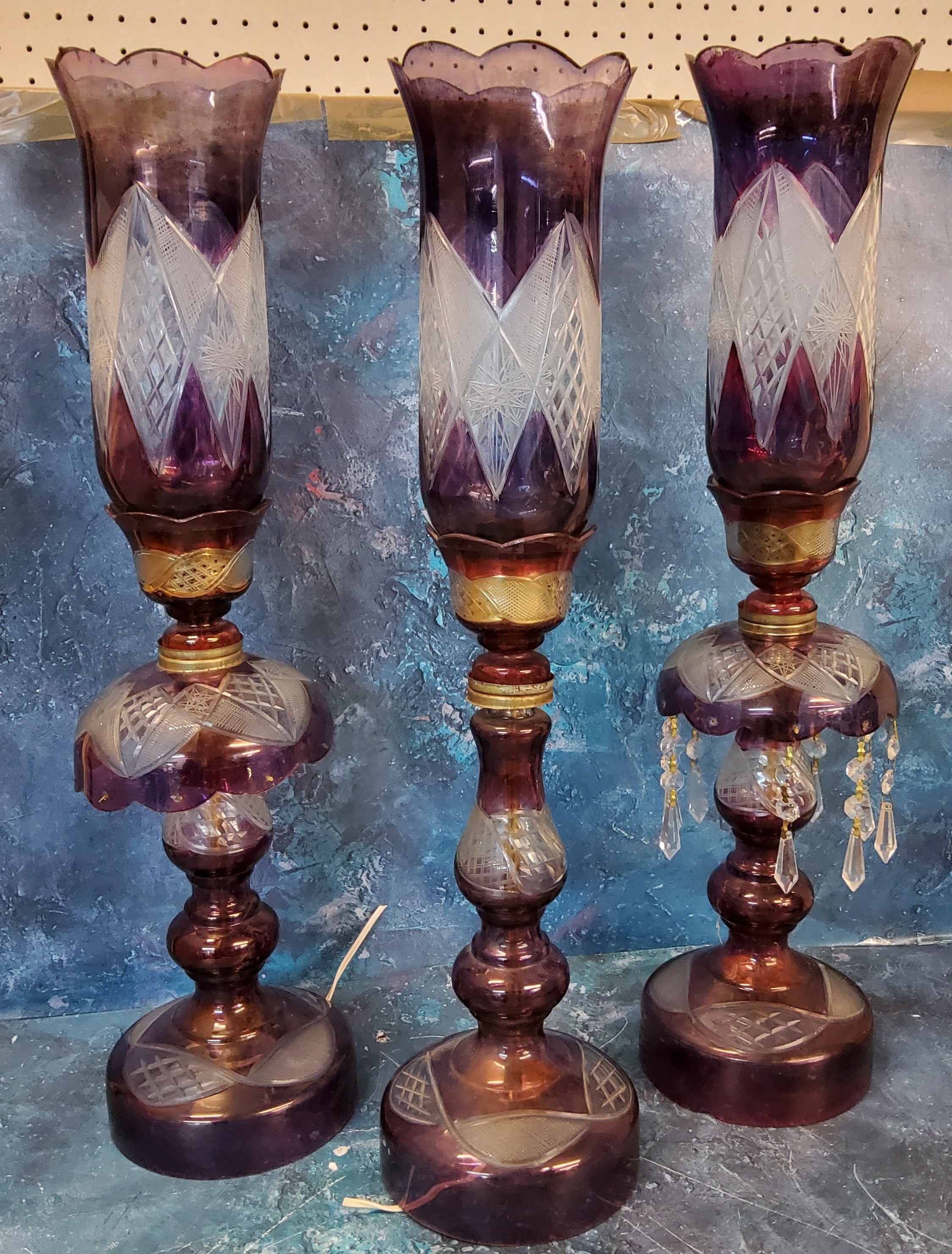 A set of three Bohemian amethyst glass storm lamps, cut with lozenges, 59cm high, early 20th century