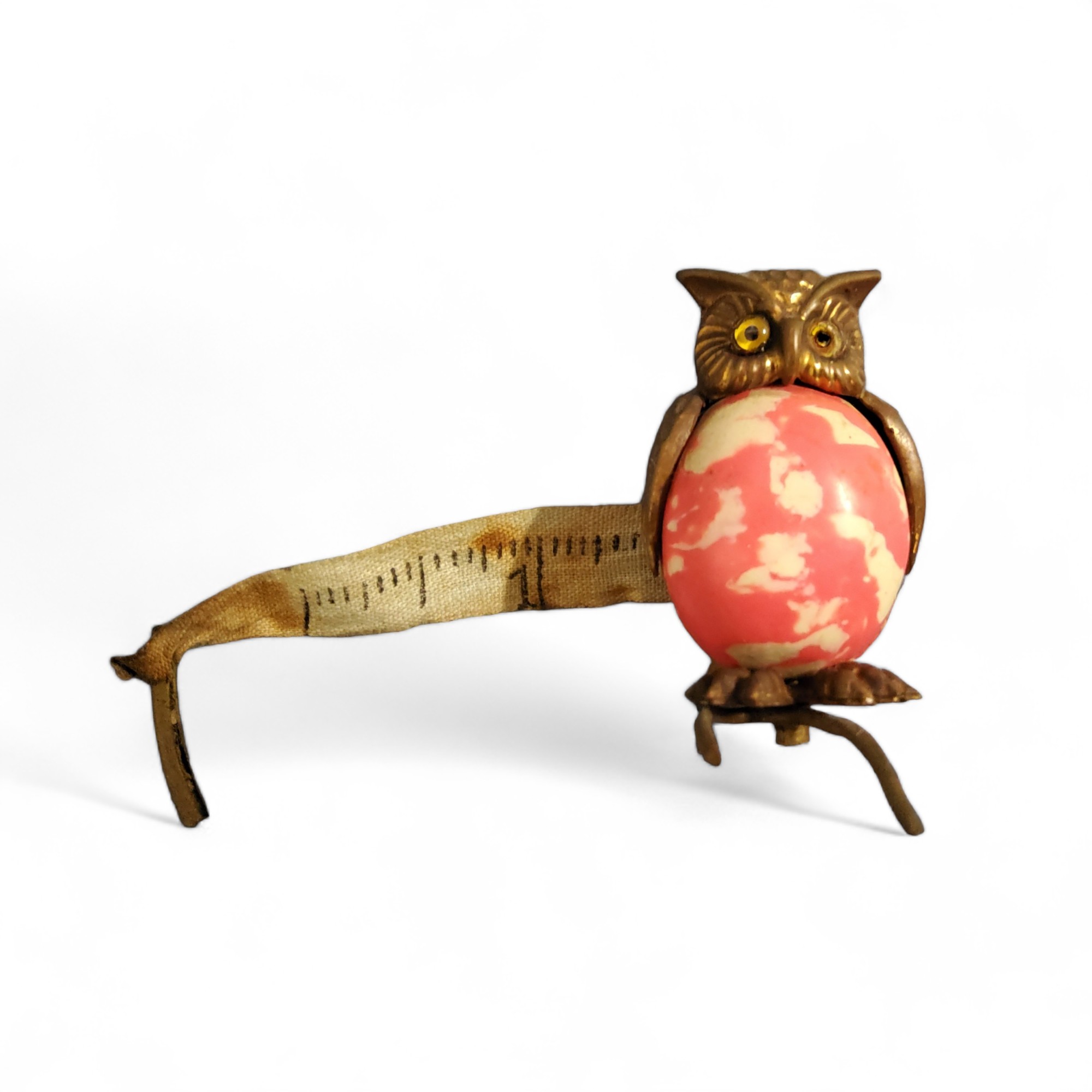 An Edwardian novelty tape measure, as an owl, 'marbled' pink body, 4.25cm high, c.1910