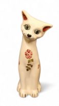 A C.H. Brannnam (Barnstaple) pottery cat,  seated, with head tilted, painted with stylised