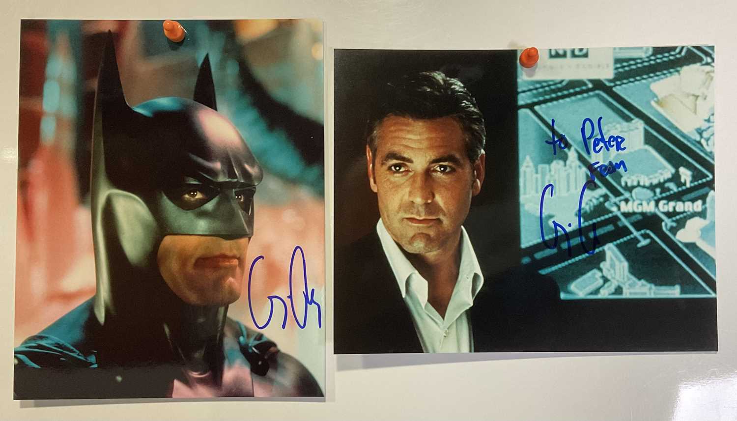 Two signed photographic stills of GEORGE CLOONEY (One as Batman) signed in blue pen, one