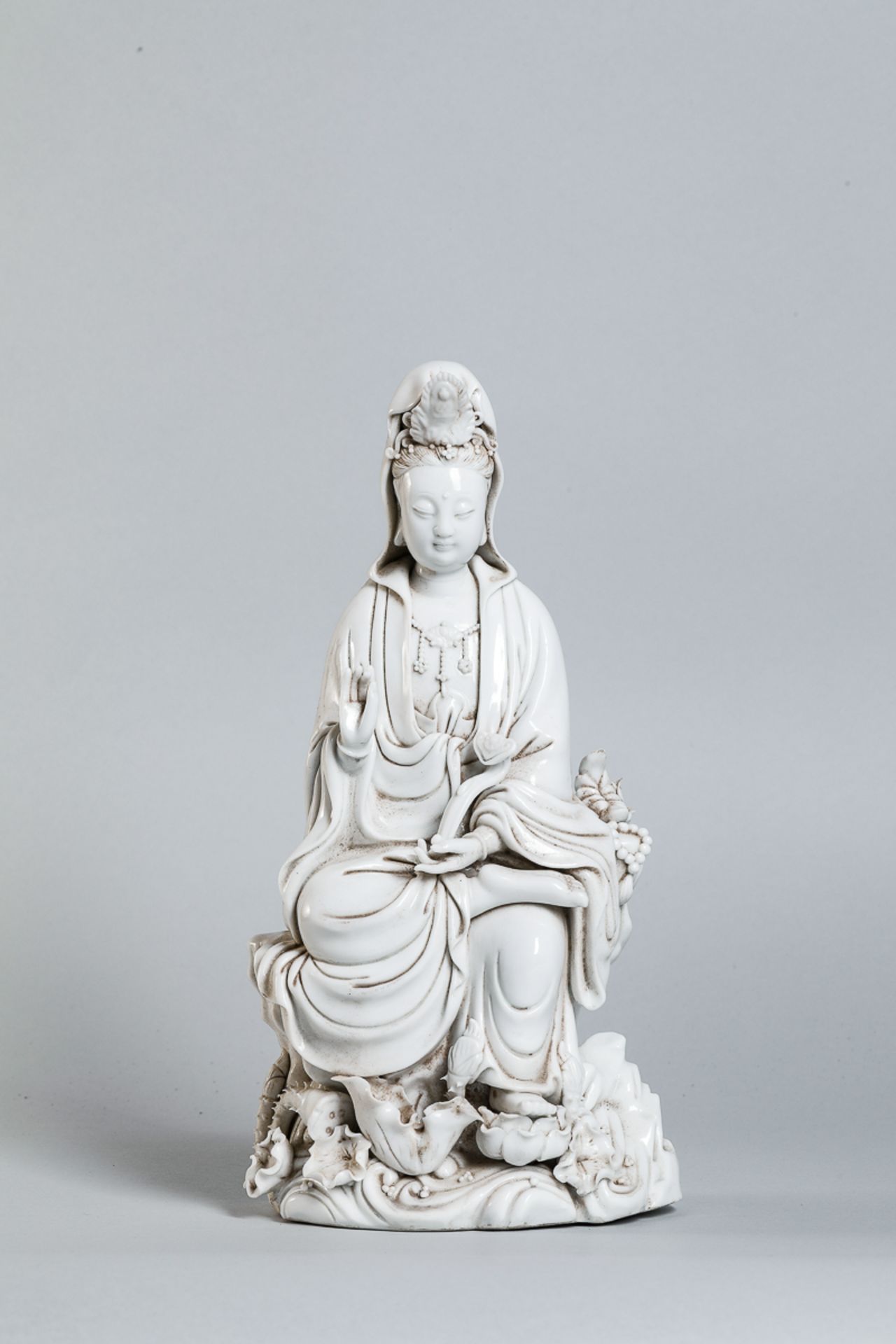 Le Boddhisattva Kwan Yin assis en délassement sur un tertre rocailleux, vêtu de la robe monastique