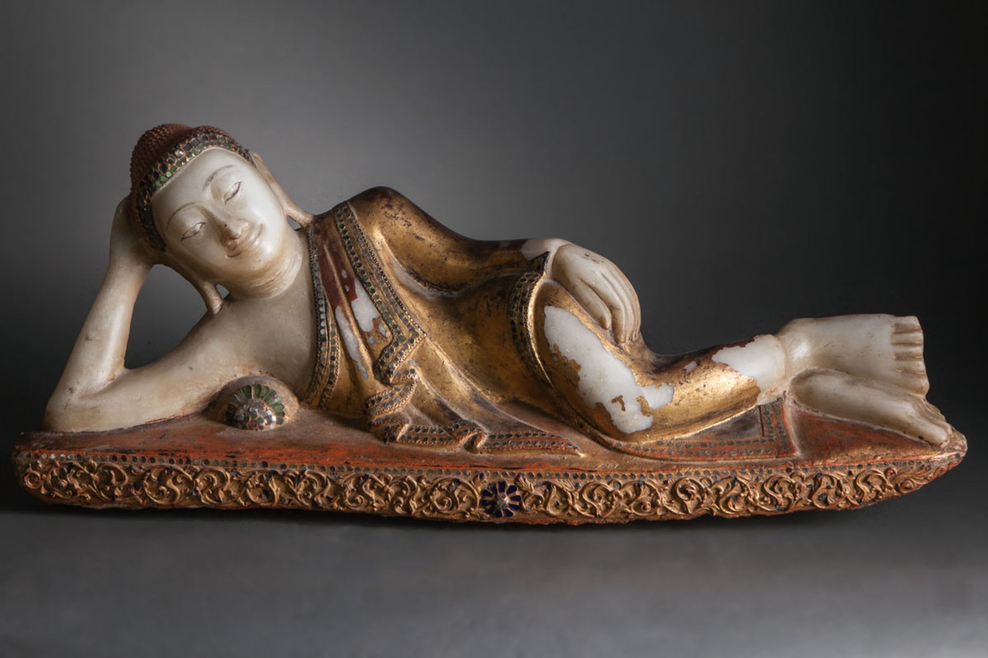 Parinirvâna Buddha allongé la tête reposant sur son bras accoudé vêtu d'une robe monastique plissée,