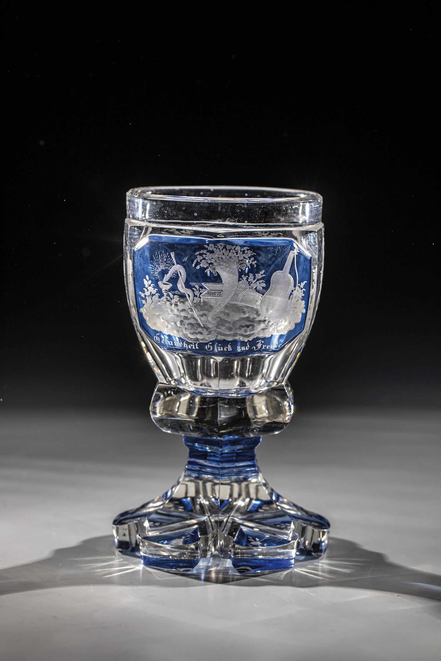 Colourless, partly blue glazed glass. Six-pass foot. Underside with engraved floral decoration.