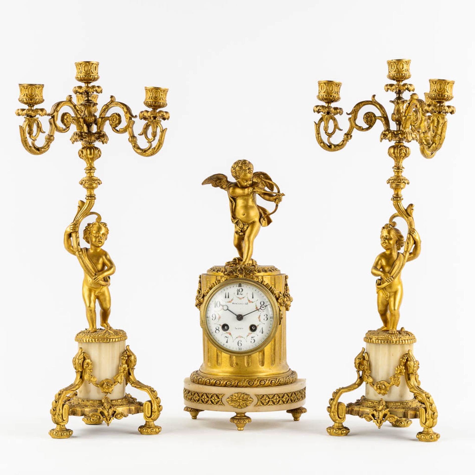 A three-piece Neoclassical mantle garniture, clock with candelabra, Cupid and Putti. 19th C. (L:13 x