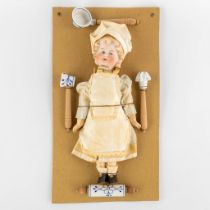 William Goebel, 'Boy Chef' a porcelain doll mounted on a cardboard with accessories. (W:20,5 x H:37