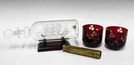 Glass ship in a bottle, two cranberry glass night light holders and a small brass telescope, 39cm