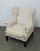 A contemporary wingback armchair, in oatmeal upholstery with silver studs and black legs, 83 x 106cm