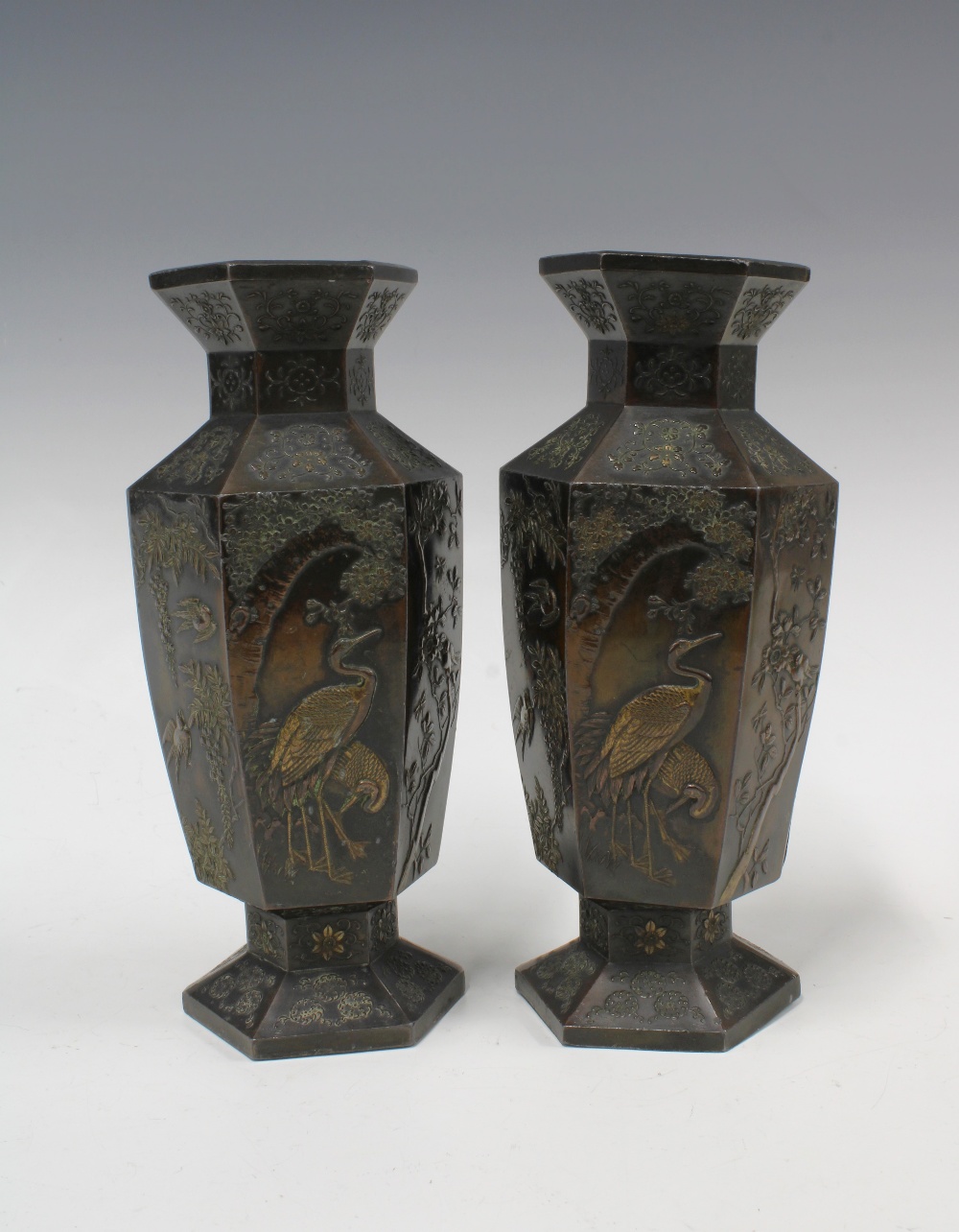 A pair of Japanese bronze patinated metal vases, hexagonal form with relief pattern of storks and