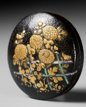 A LACQUERED WOOD MANJU NETSUKE DEPICTING CHRYSANTHEMUMS BY A FENCE