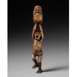 A POWERFUL WOOD NETSUKE OF A DANCING MAN WITH A DARUMA DOLL