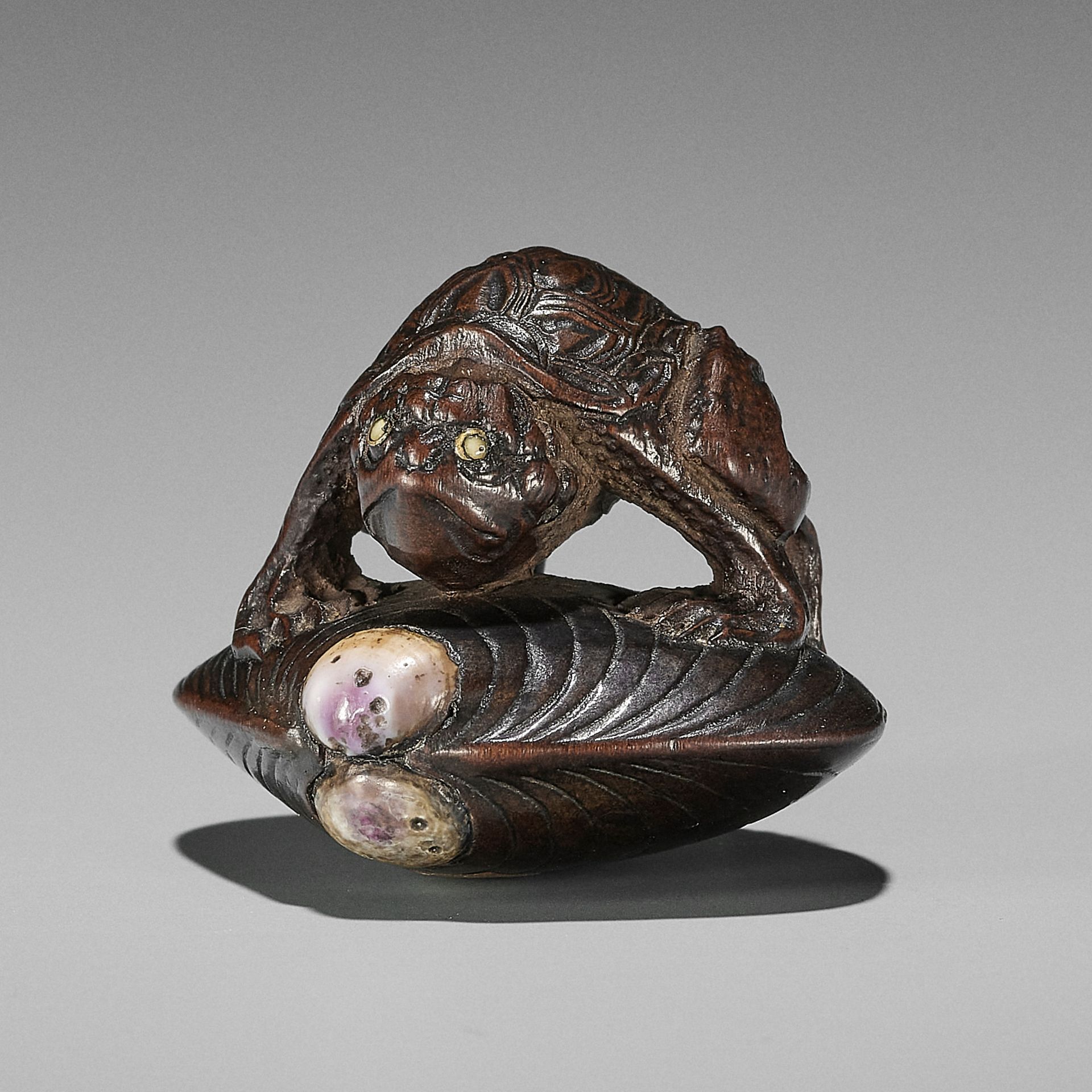 AN AMUSING INLAID WOOD NETSUKE OF A KAPPA ON HAMAGURI CLAM