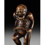 TOUN: AN AMUSING WOOD NETSUKE OF A NAKED MAN TYING HIS FUNDOSHI