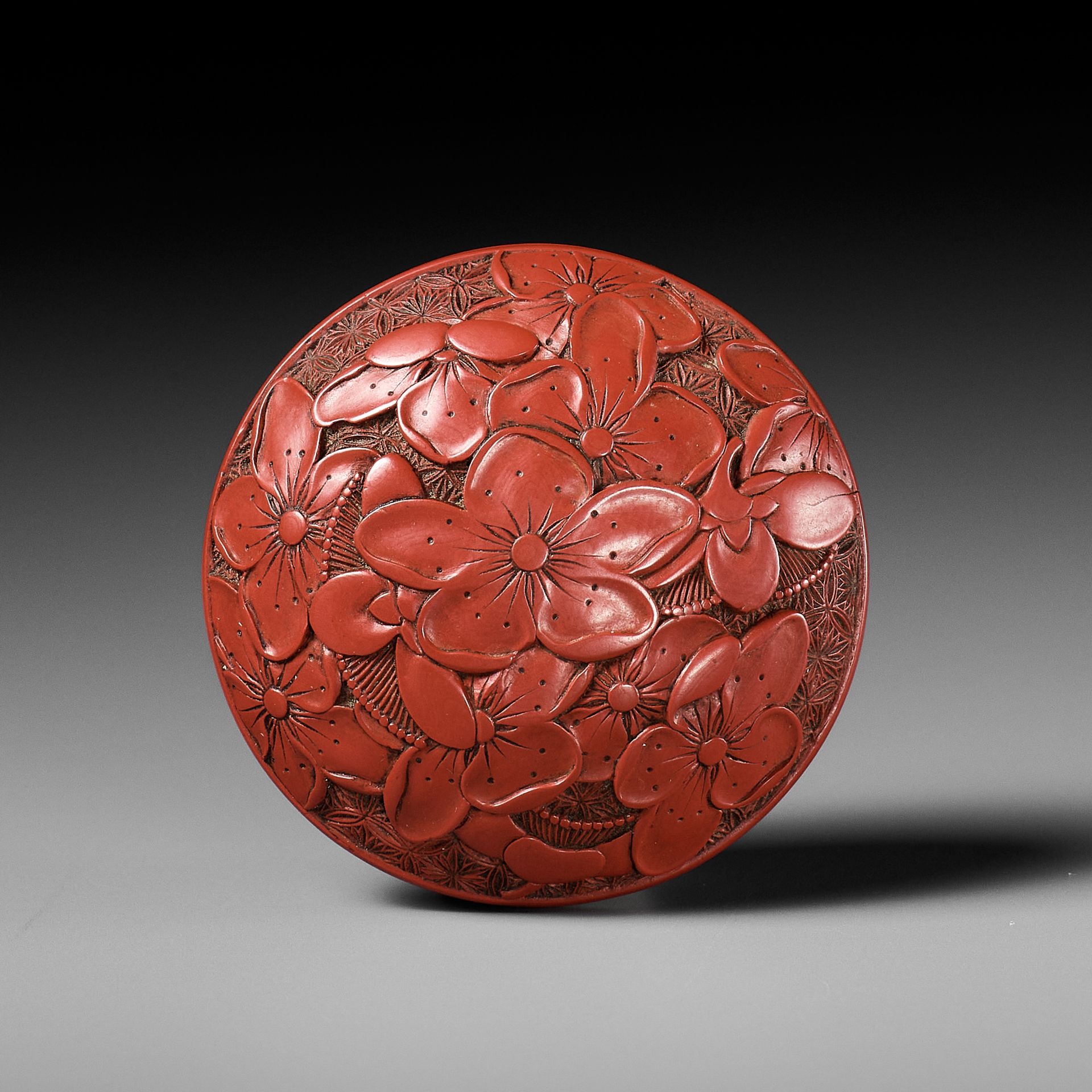 A FINE TSUISHU (CARVED RED LACQUER) MANJU NETSUKE WITH PEACH BLOSSOMS