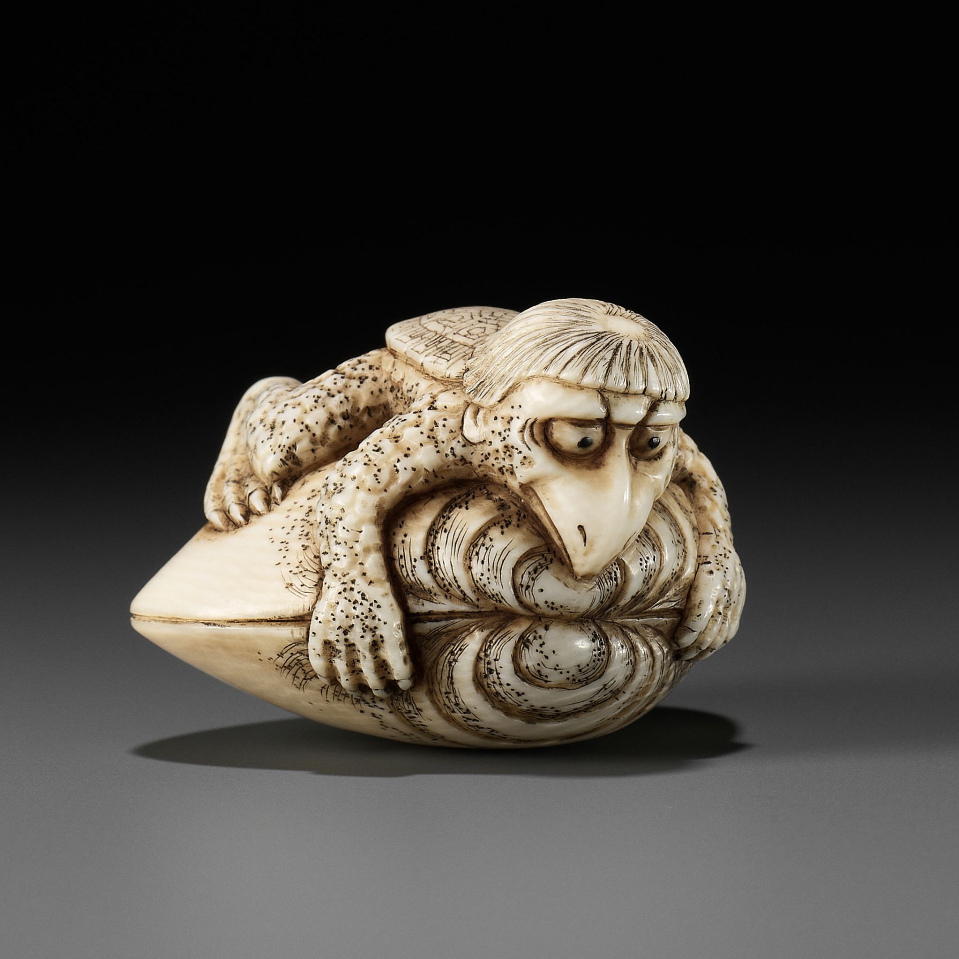 AN IVORY NETSUKE OF A KAPPA TRAPPED BY A HAMAGURI CLAM