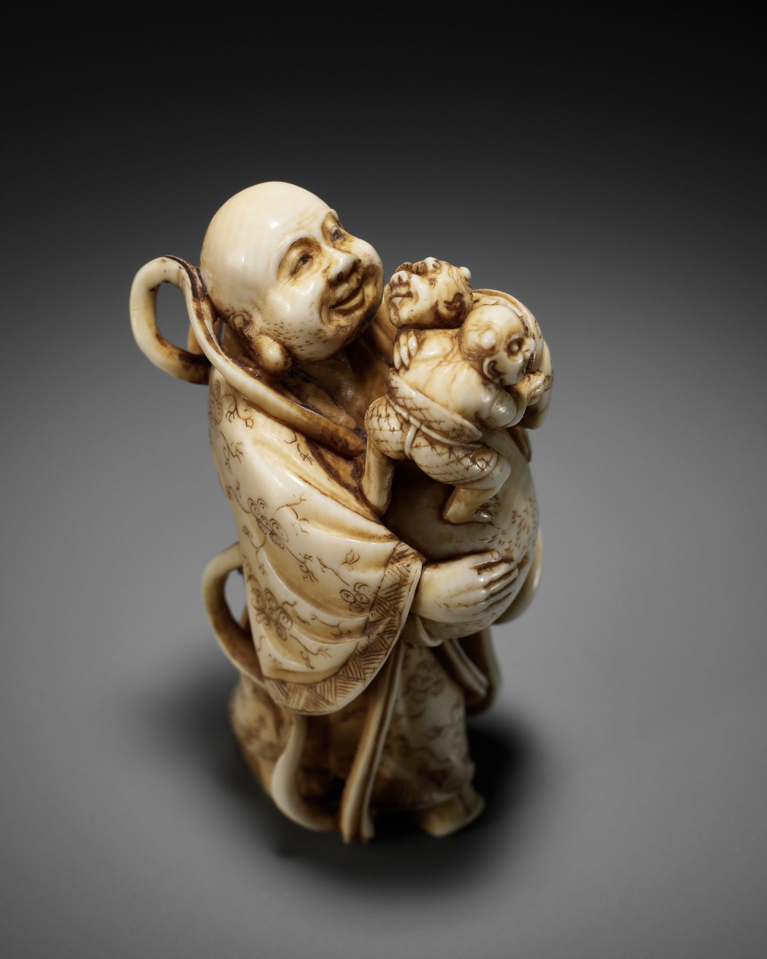 GYOKUZAN: AN AMUSING IVORY NETSUKE OF HOTEI WITH WRESTLING ONI