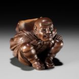 SOKYU: A FINE SO SCHOOL WOOD NETSUKE OF A MAN CARRYING A LARGE TENGU MASK