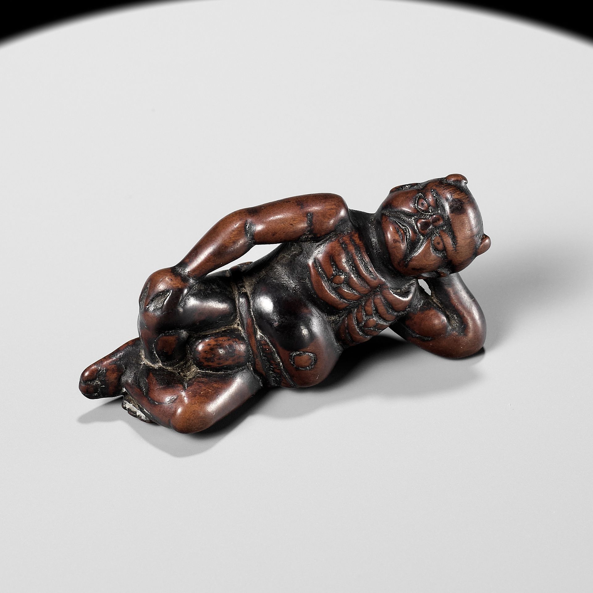 A RARE WOOD NETSUKE OF A RECLINING ONI