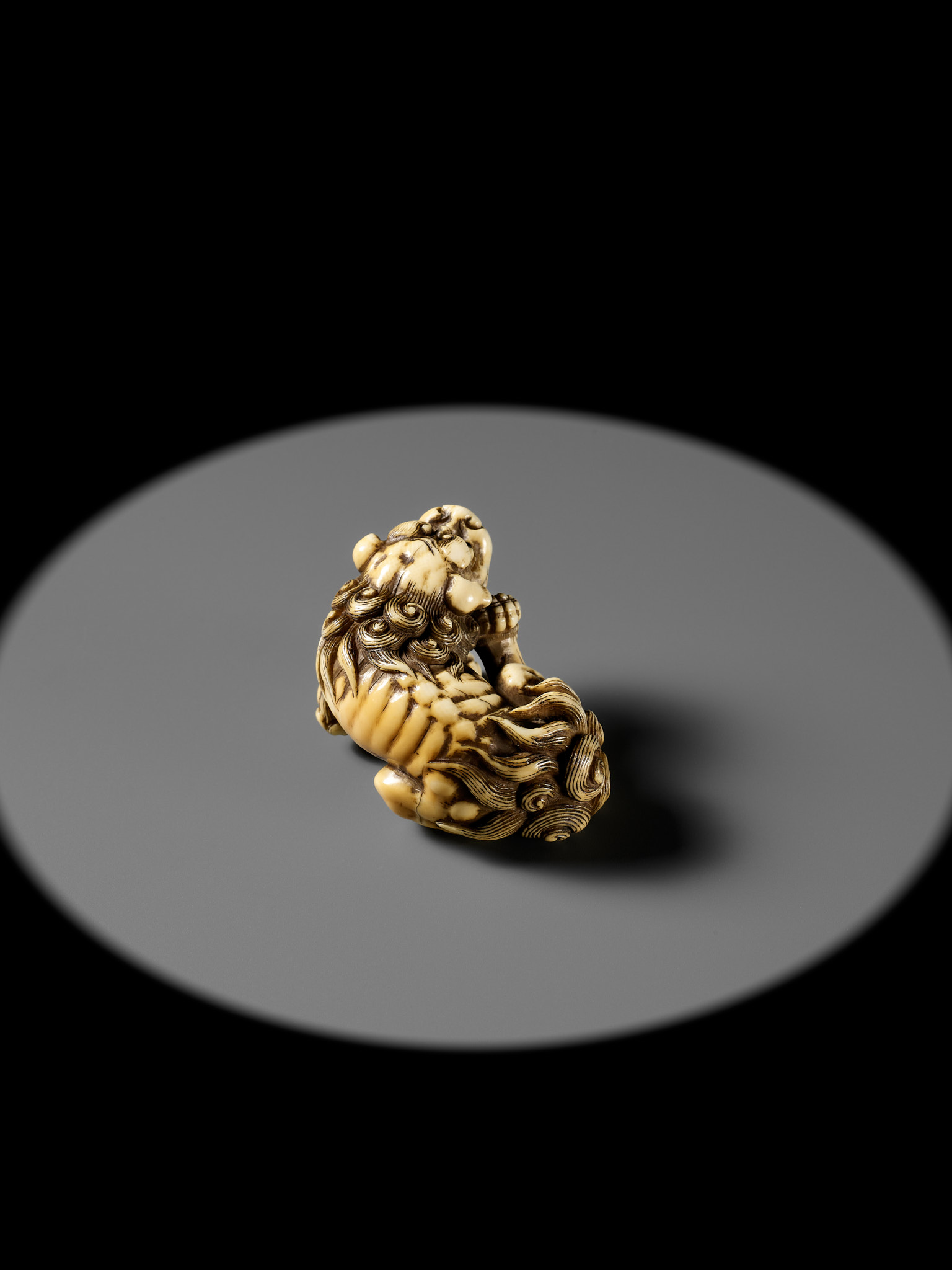 TOMOTADA: A SUPERB IVORY NETSUKE OF A RECUMBENT SHISHI SCRATCHING ITS JOWL - Image 15 of 24