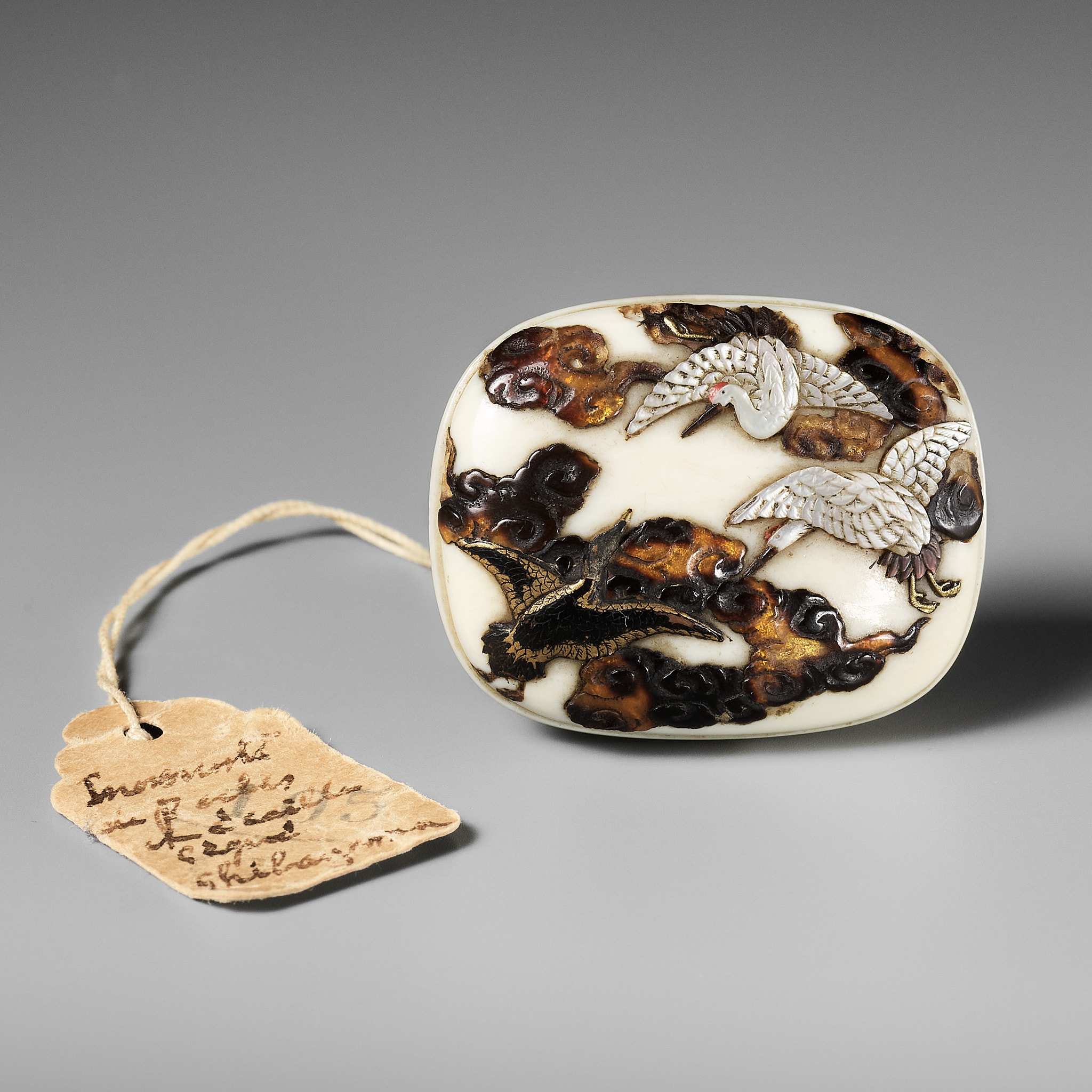 SHIBAYAMA: A FINE LACQUERED AND INLAID IVORY MANJU NETSUKE DEPICTING CRANES AND CLOUDS