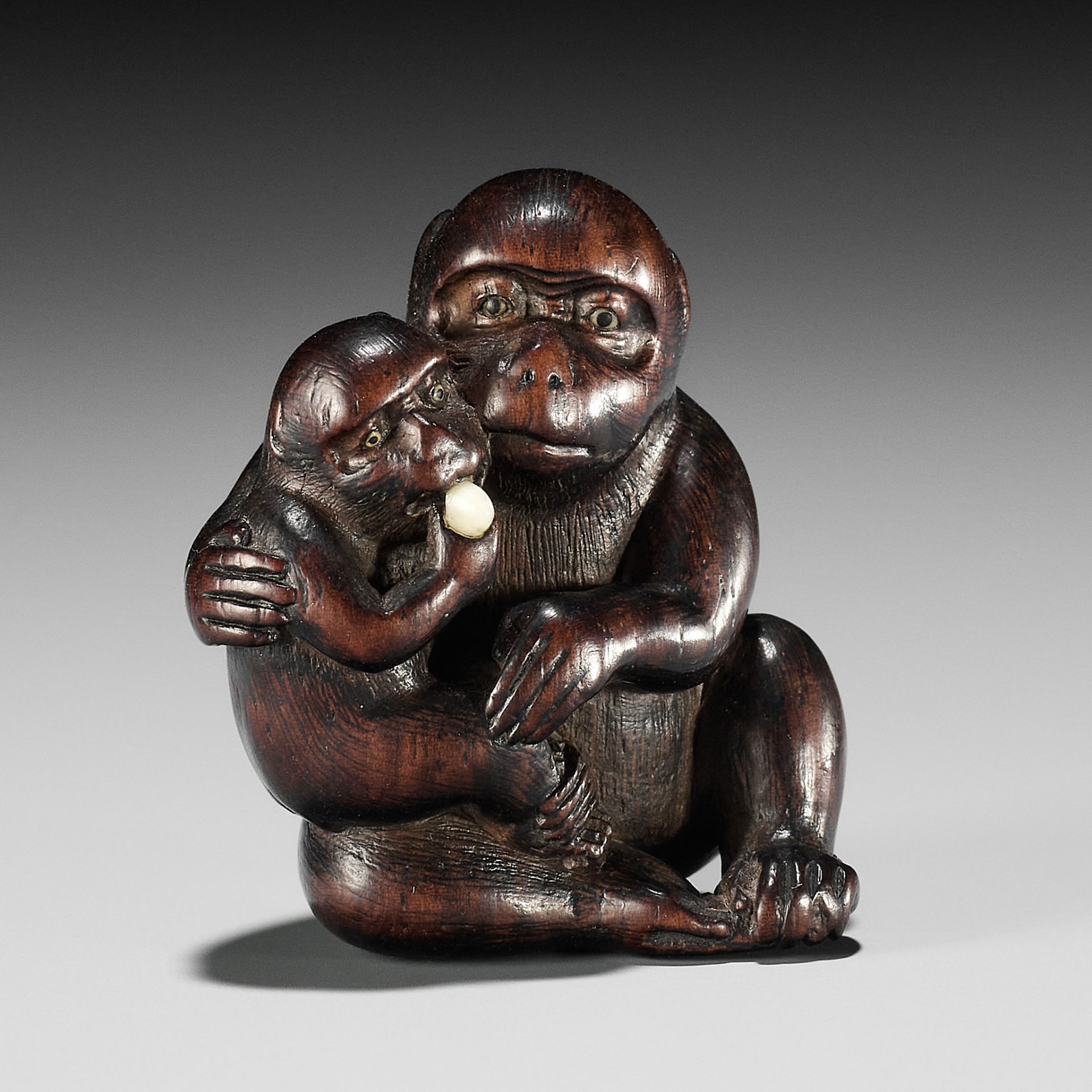 HIDECHIKA: A CHARMING INLAID WOOD NETSUKE OF A MONKEY FEEDING YOUNG