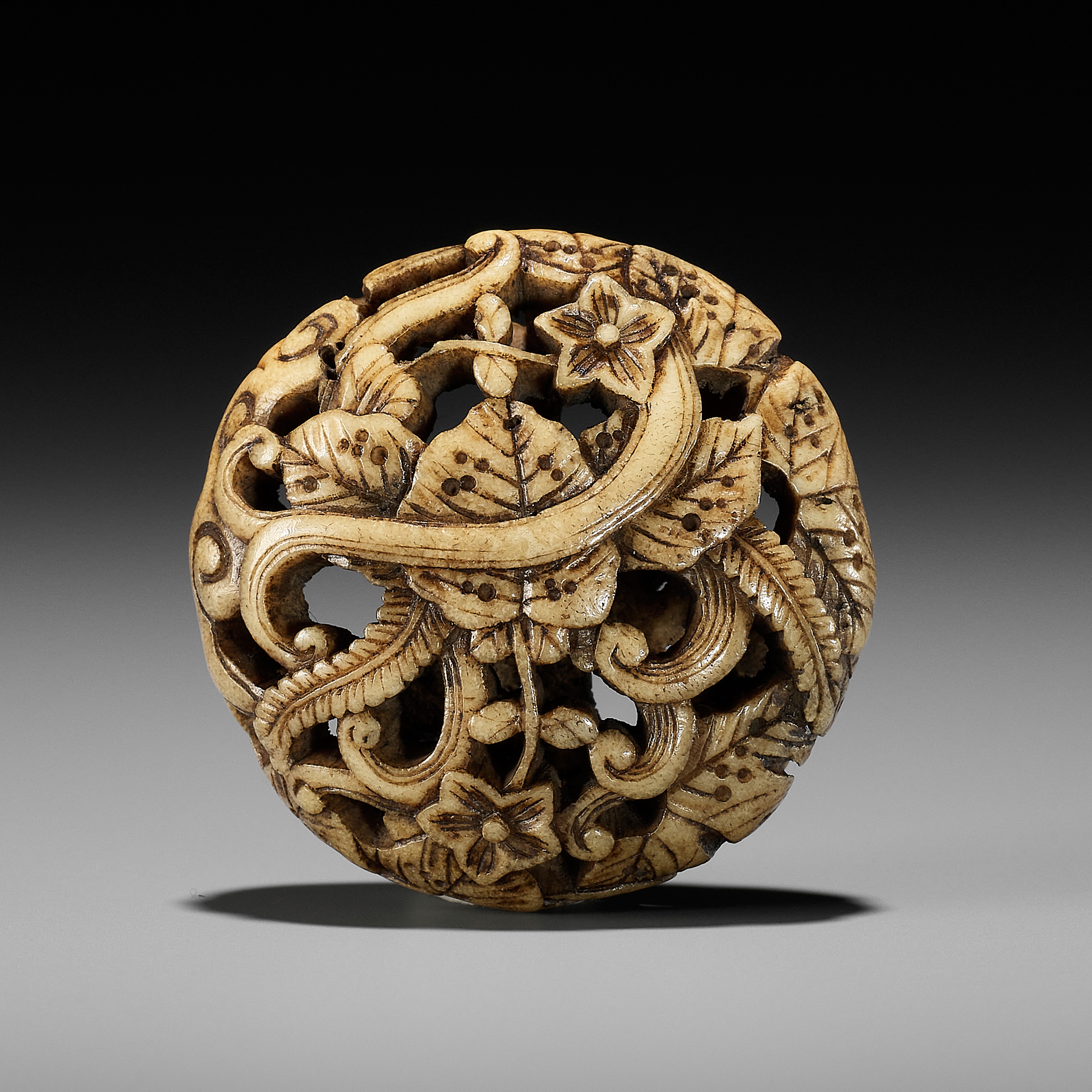 AN ANTLER RYUSA MANJU NETSUKE WITH FLORAL DESIGN