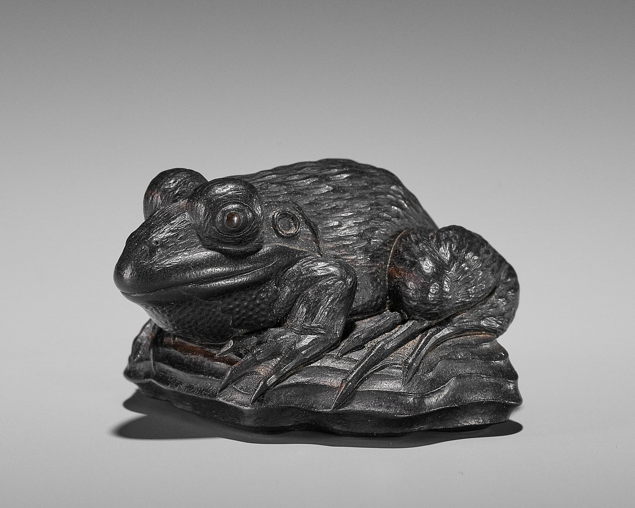 A SUPERB EBONY WOOD NETSUKE OF A FROG ON DRIFTWOOD ATTRIBUTED TO SEIYODO TOMIHARU