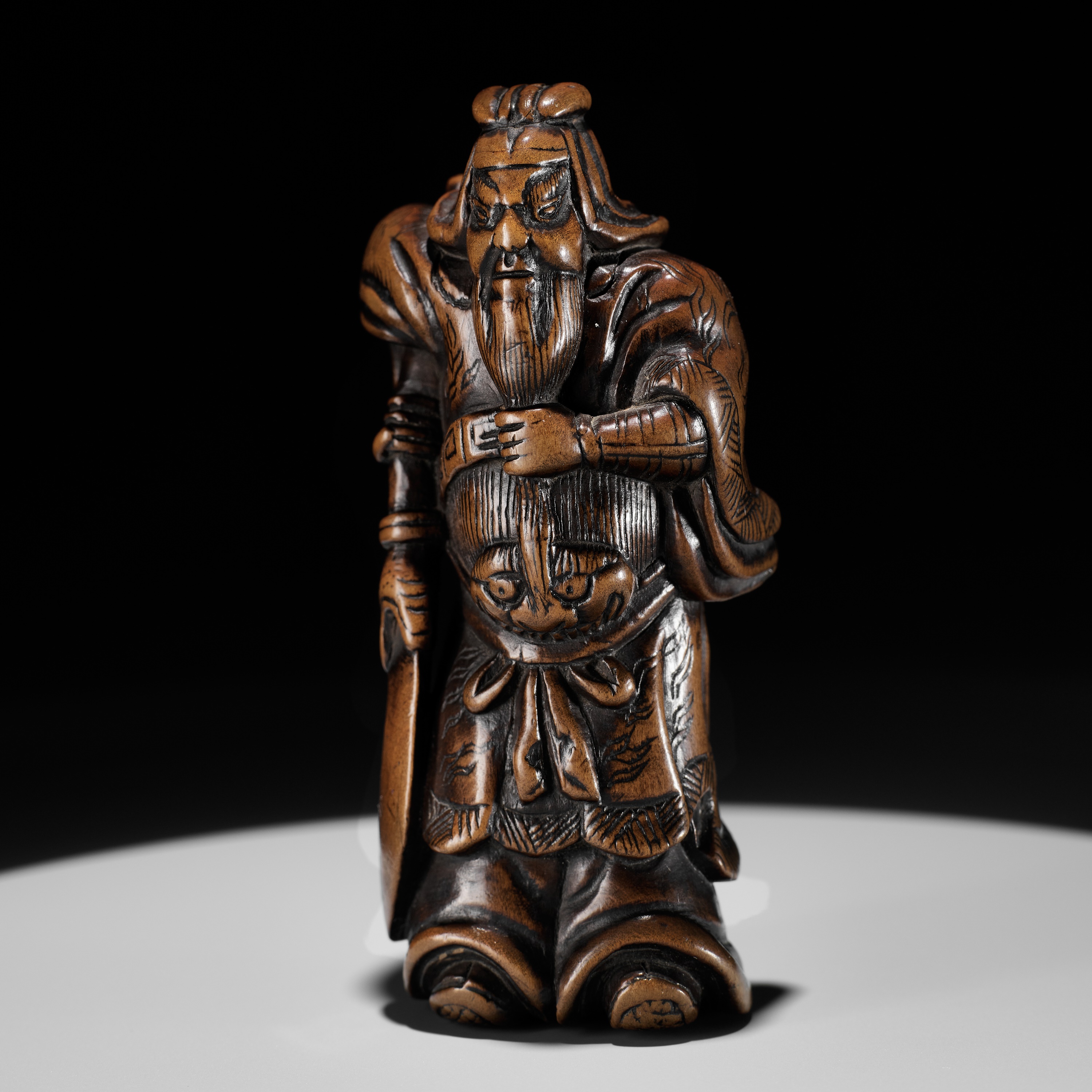 A POWERFUL WOOD NETSUKE OF KAN'U WITH HIS HALBERD