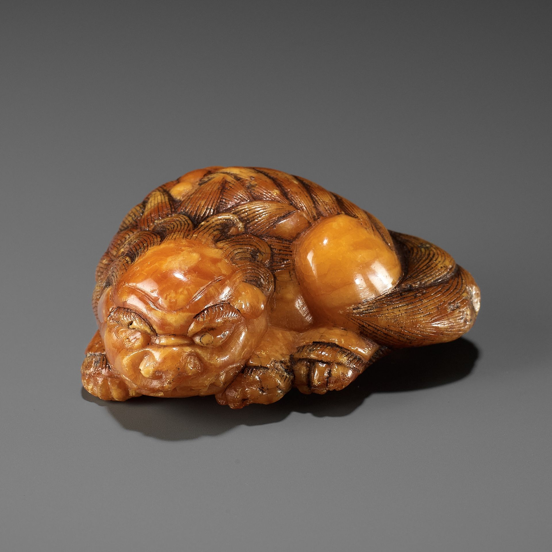 A VERY RARE CLOUDY AMBER NETSUKE OF A RECUMBENT SHISHI