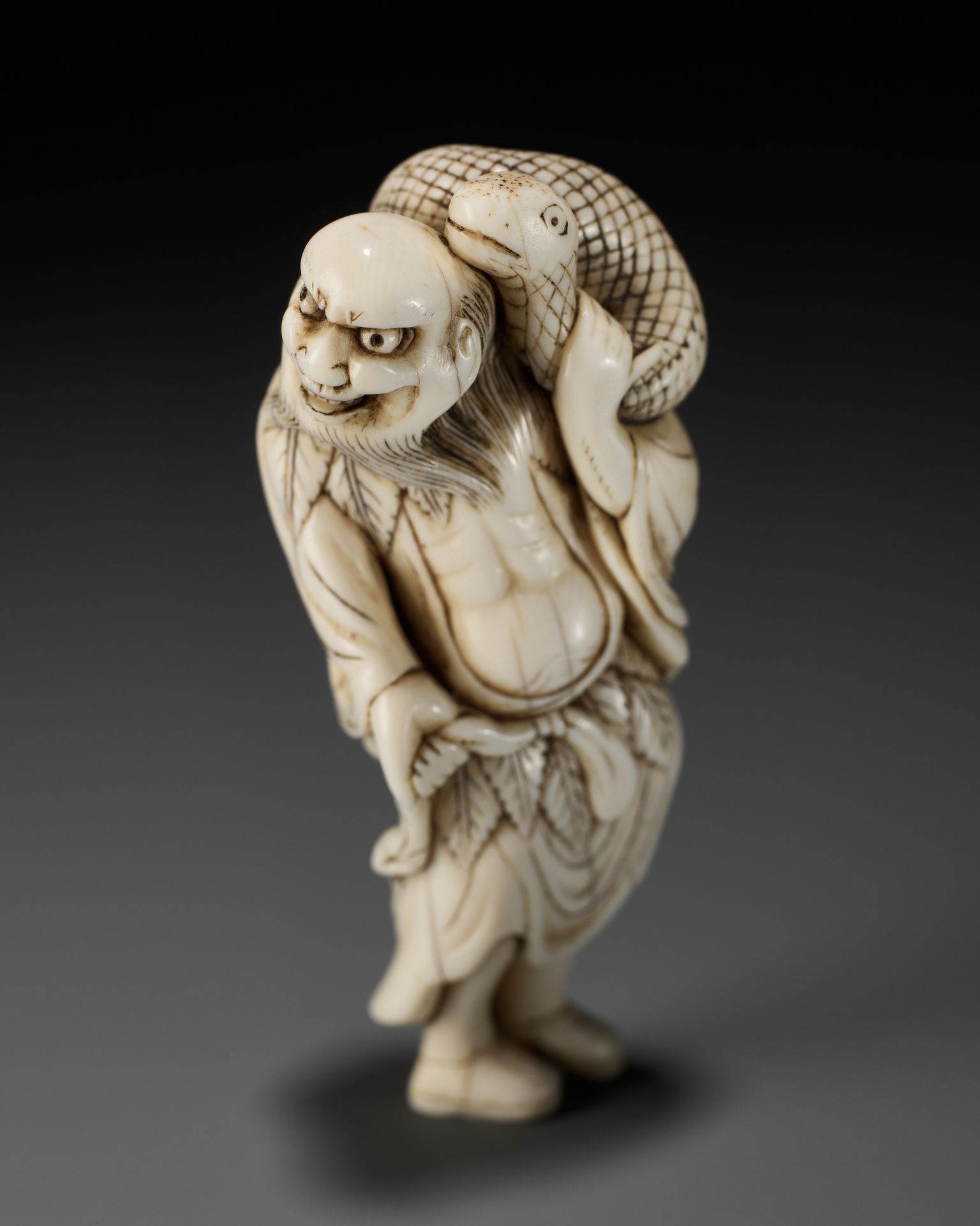 A RARE IVORY NETSUKE OF A SENNIN WITH A SNAKE