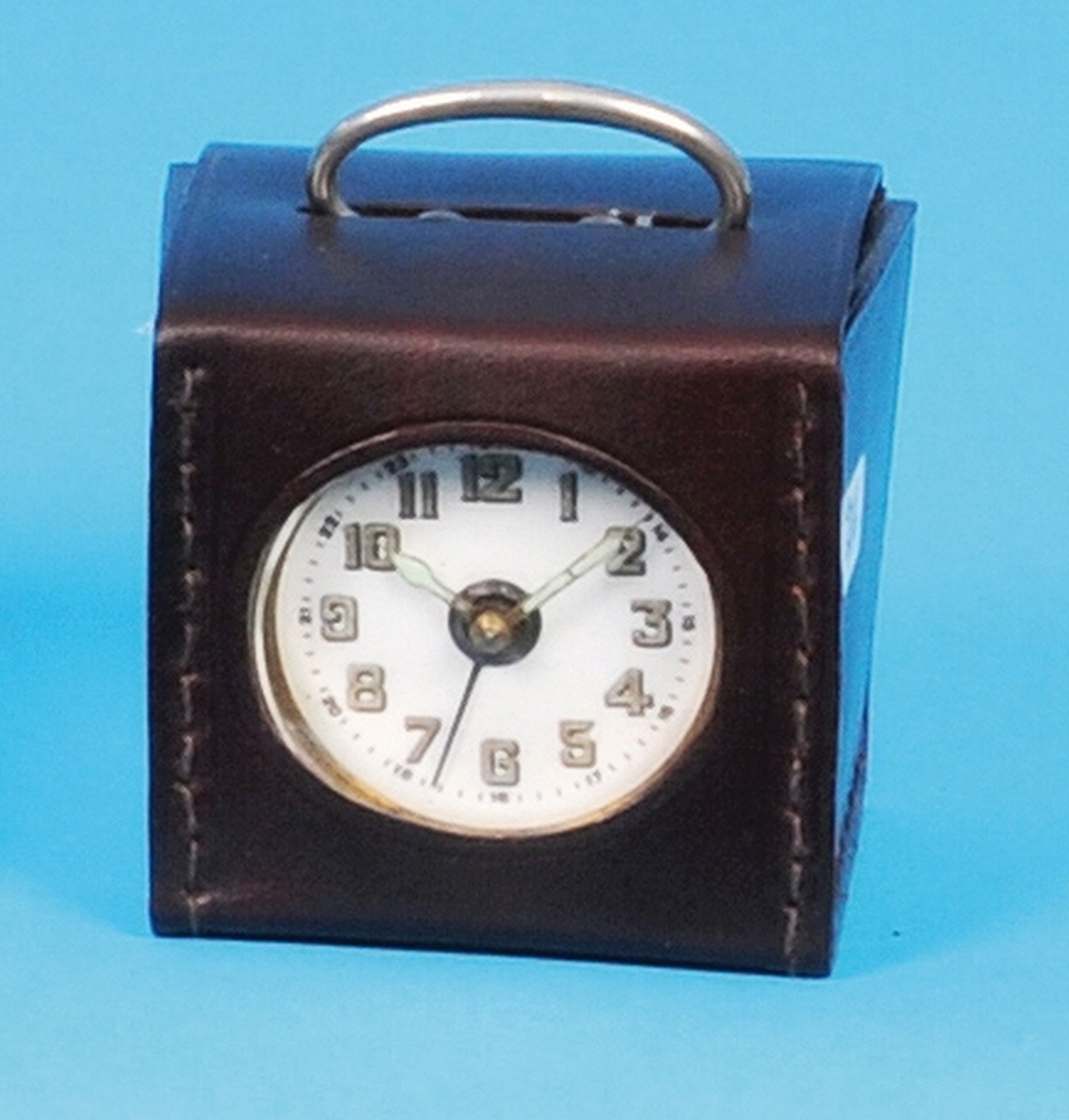 Small square alarm clock in original case, carrying bracket serves also for setting off alarm clocks