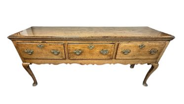 An 18th Century oak dresser base with three drawers above a shaped frieze on cabriole front legs,