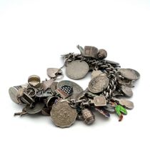 A silver charm bracelet with numerous coins, charms and travel charms attached, many hallmarked or