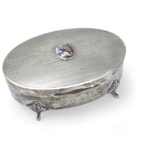 An oval silver hinged trinket box on four legs with engine turned patterned lid with a painted